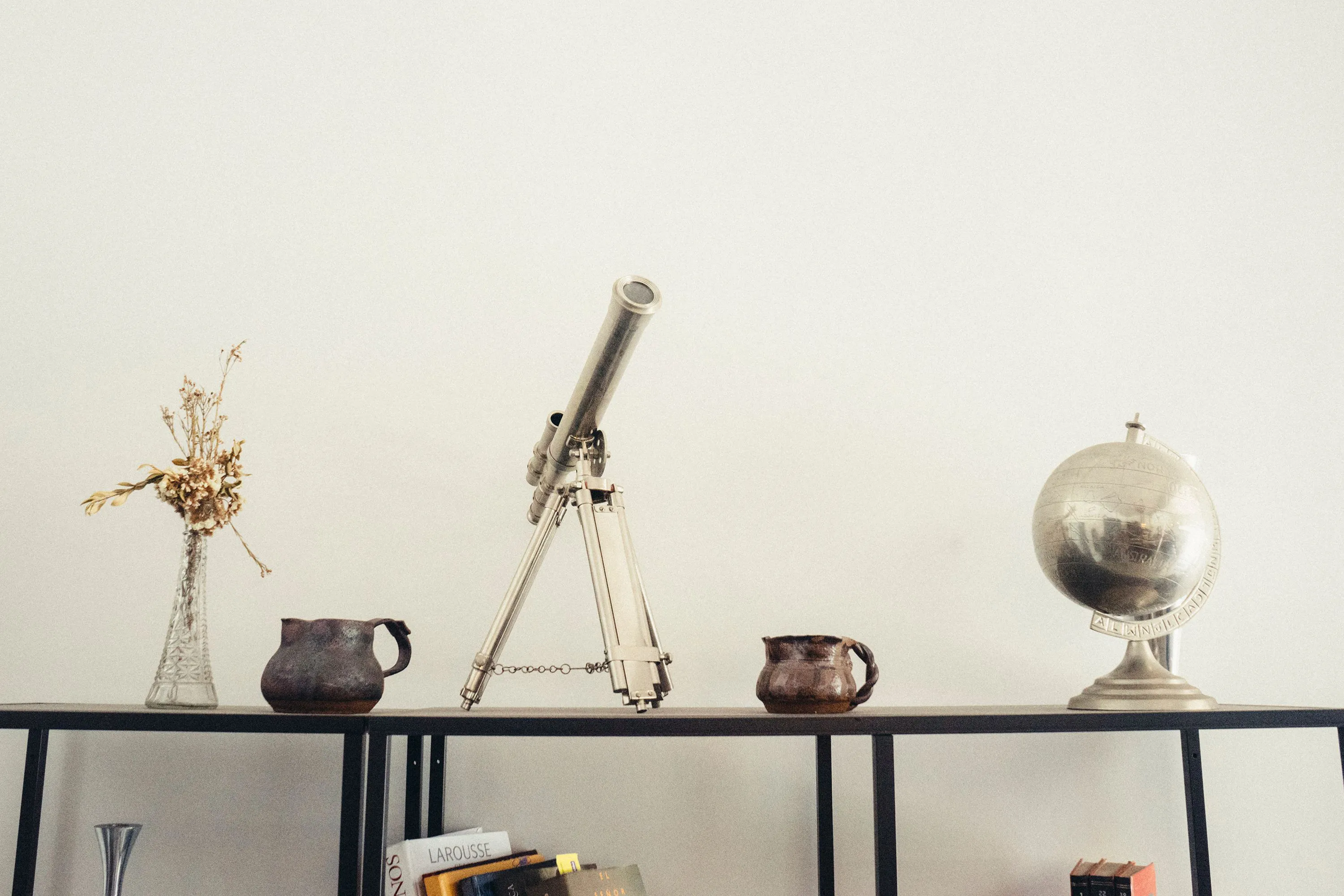 Console table styled with vintage telescope, silver globe, dried flowers, and collected ceramic vessels