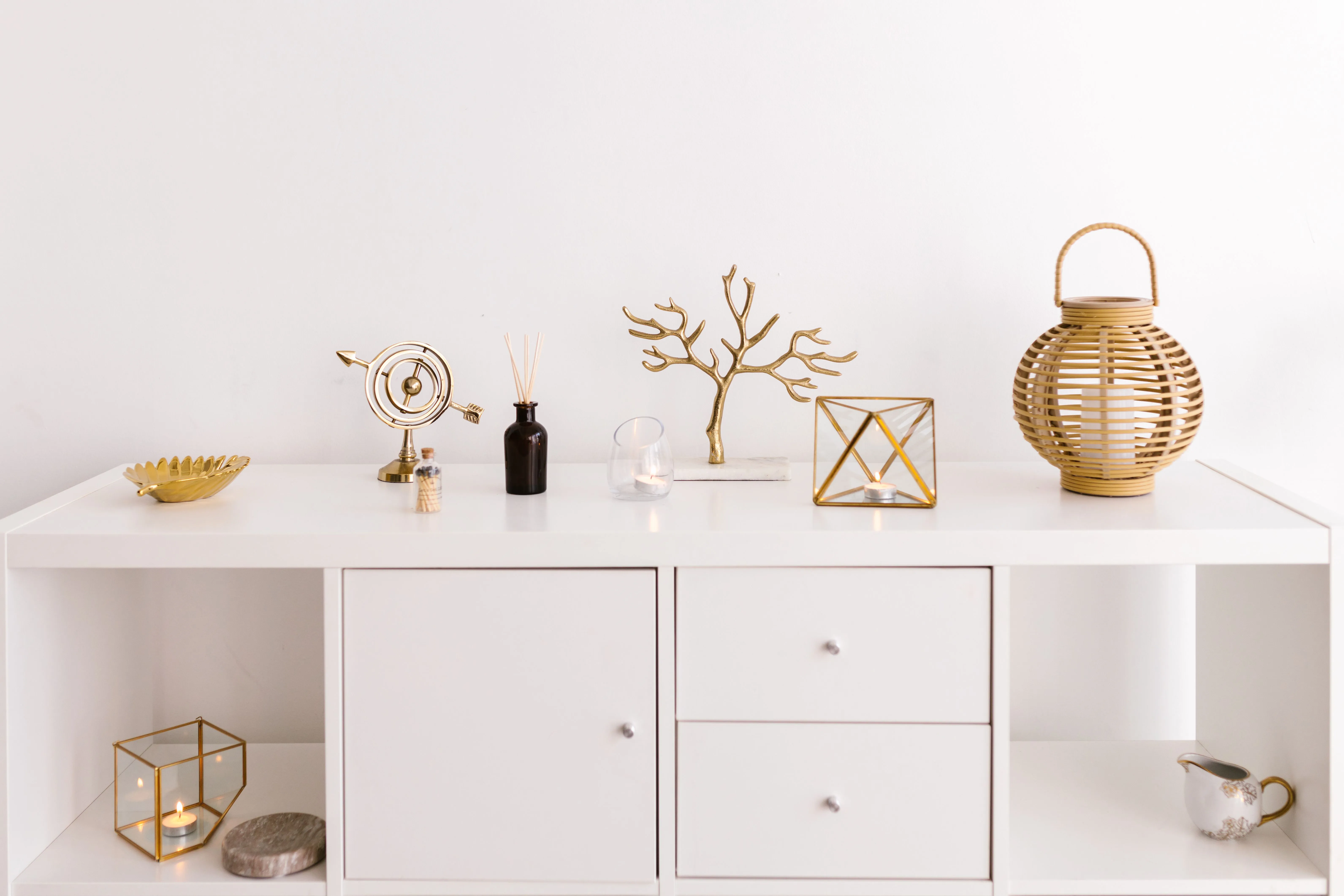 White console table styled with warm gold coral branch, geometric candle holder, and wicker lantern