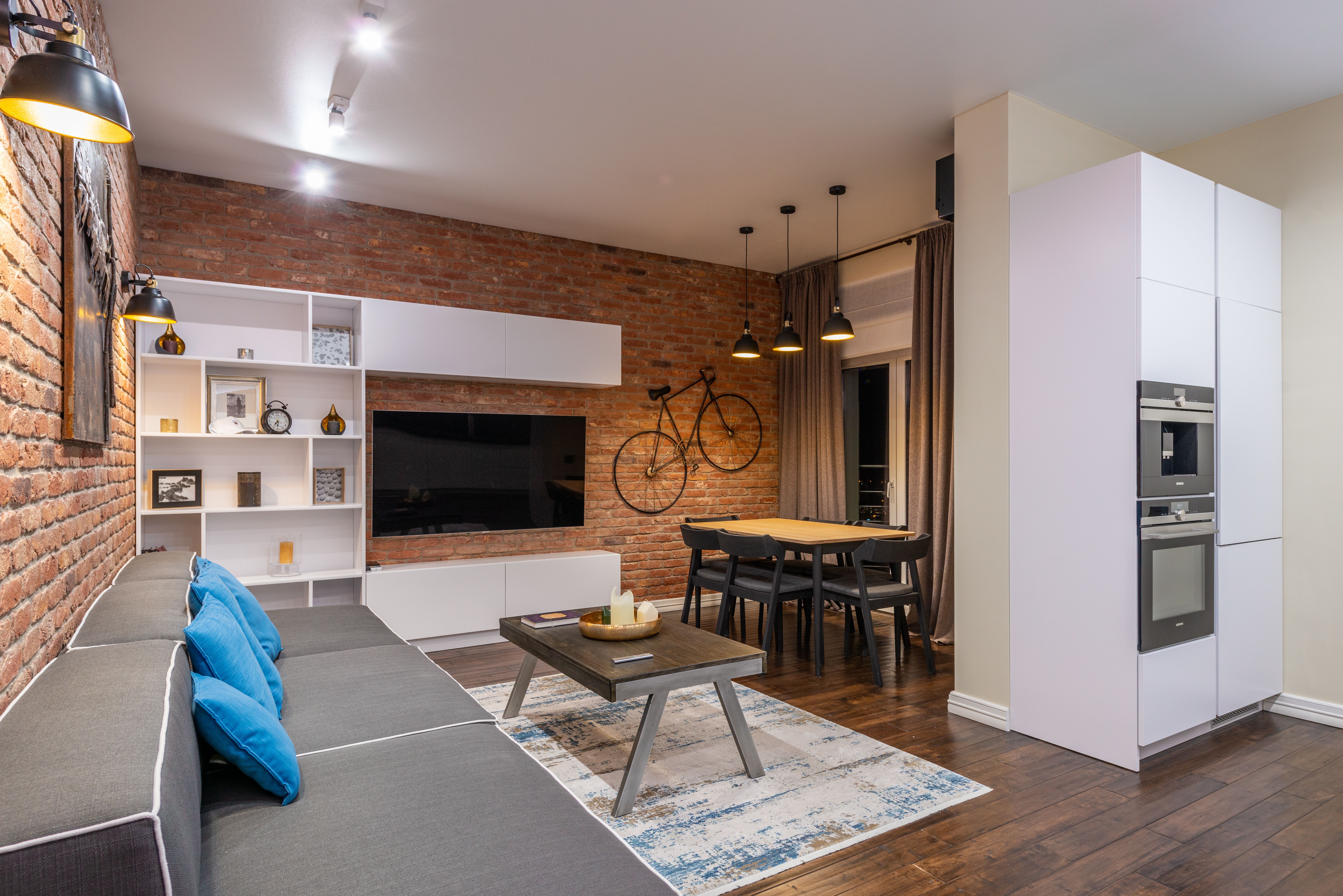 An industrial studio apartment with exposed brick, open living and dining zones, and warm pendant lighting