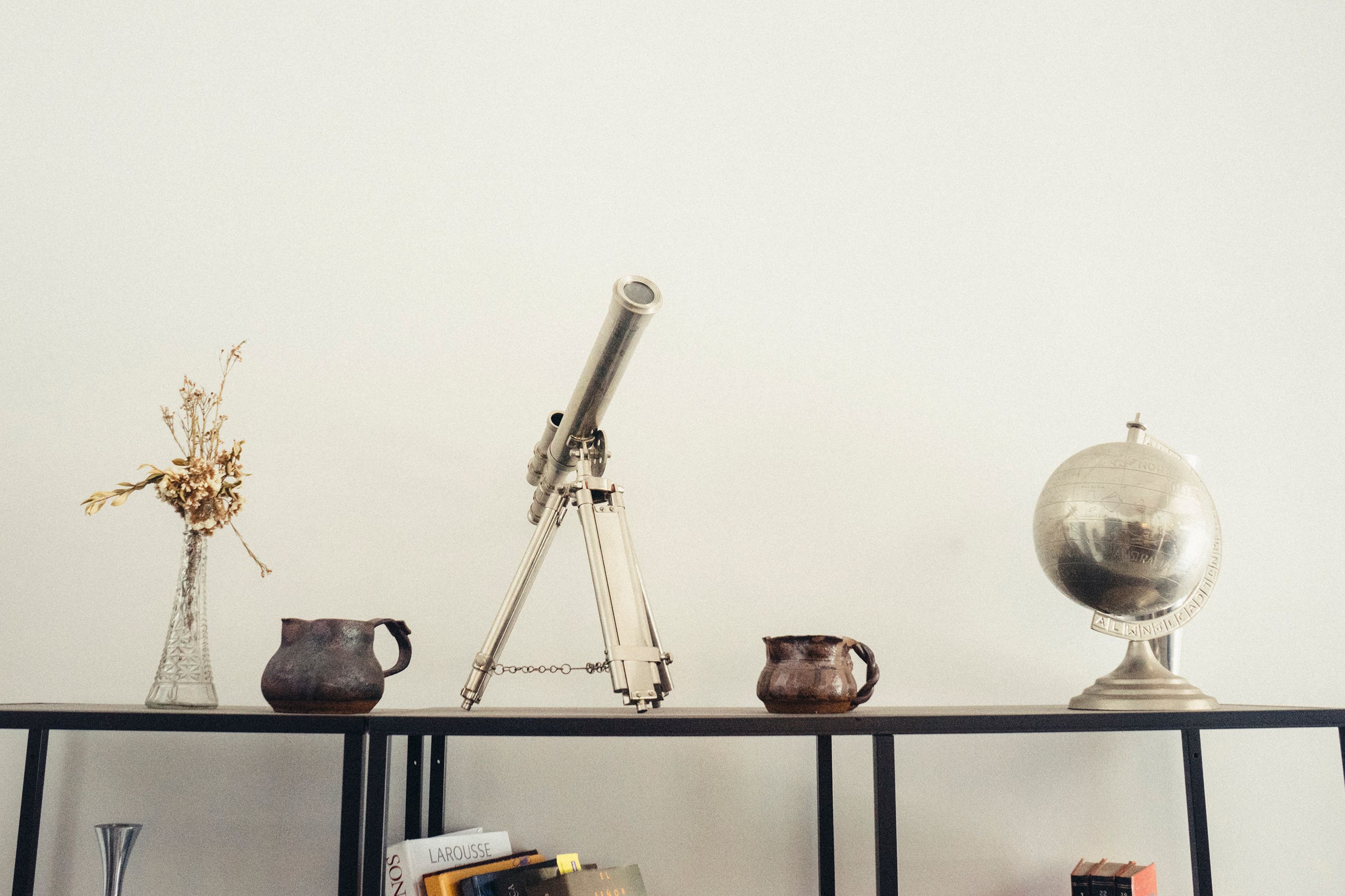 Console table styled with vintage telescope, silver globe, dried flowers, and collected ceramic vessels