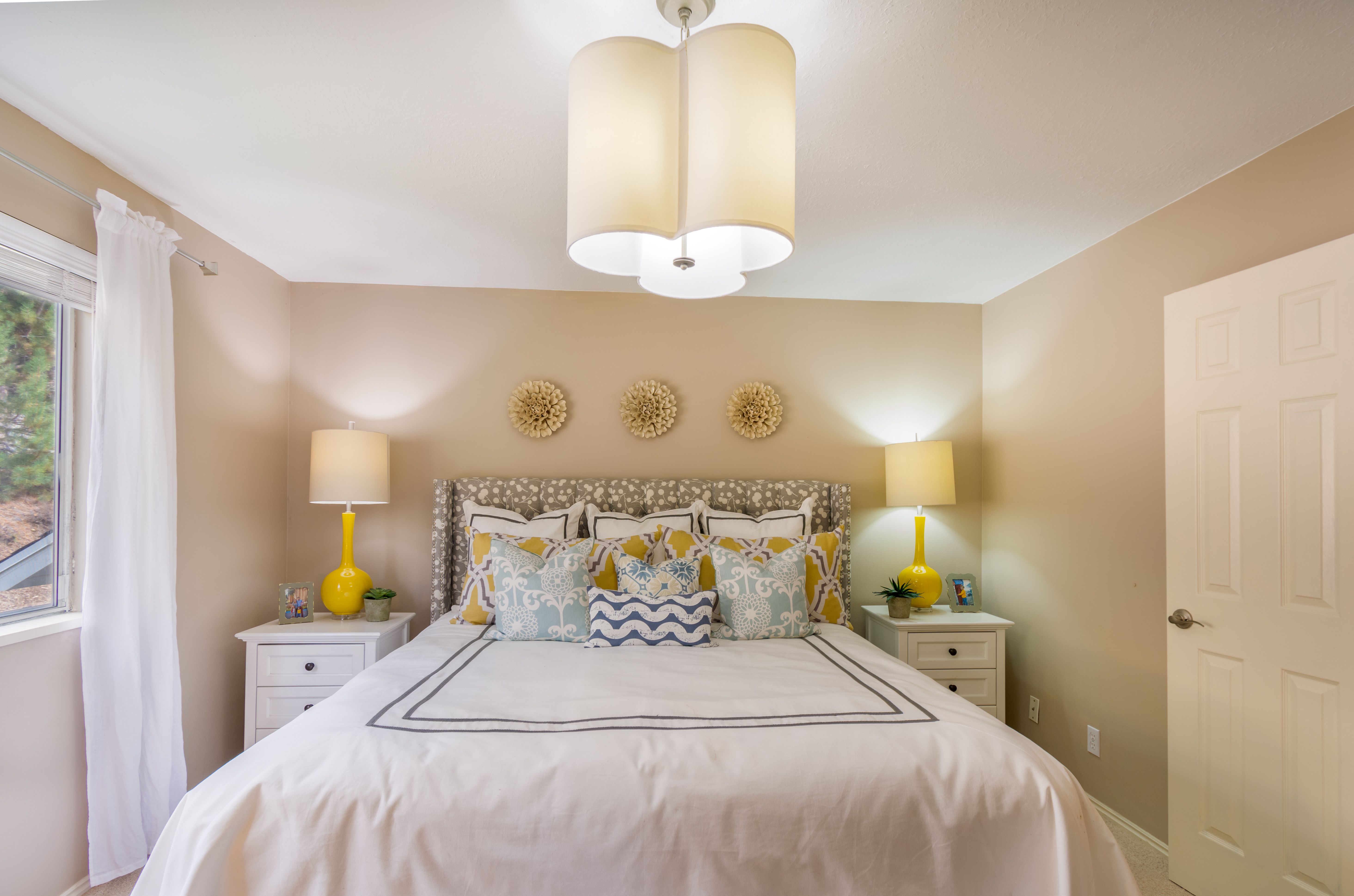 Bed with layered patterned pillows in yellow and blue, white bedding, and matching yellow lamps