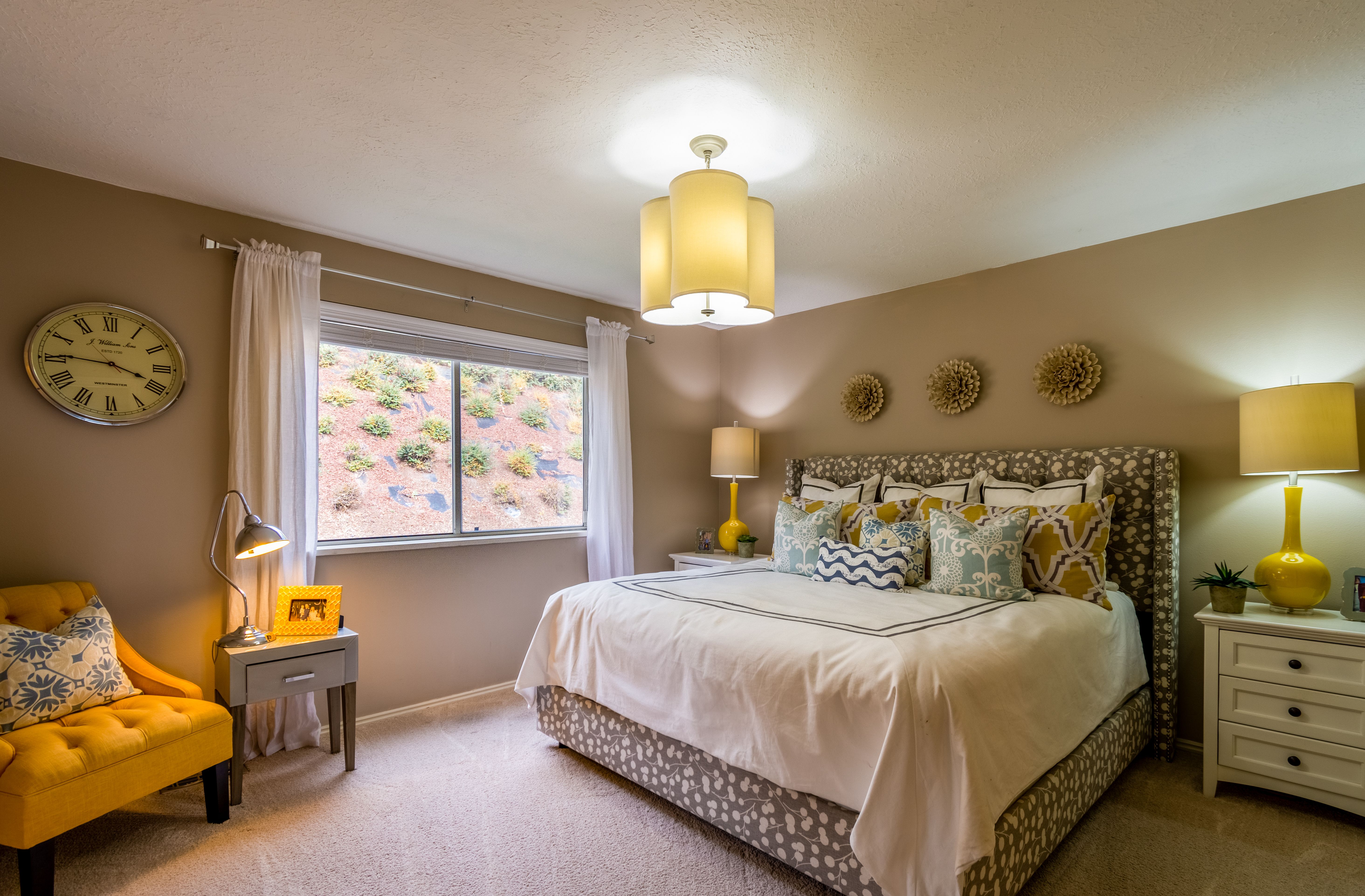 Cozy bedroom with warm yellow bedside lamps, a patterned headboard, and a soft reading chair by the window