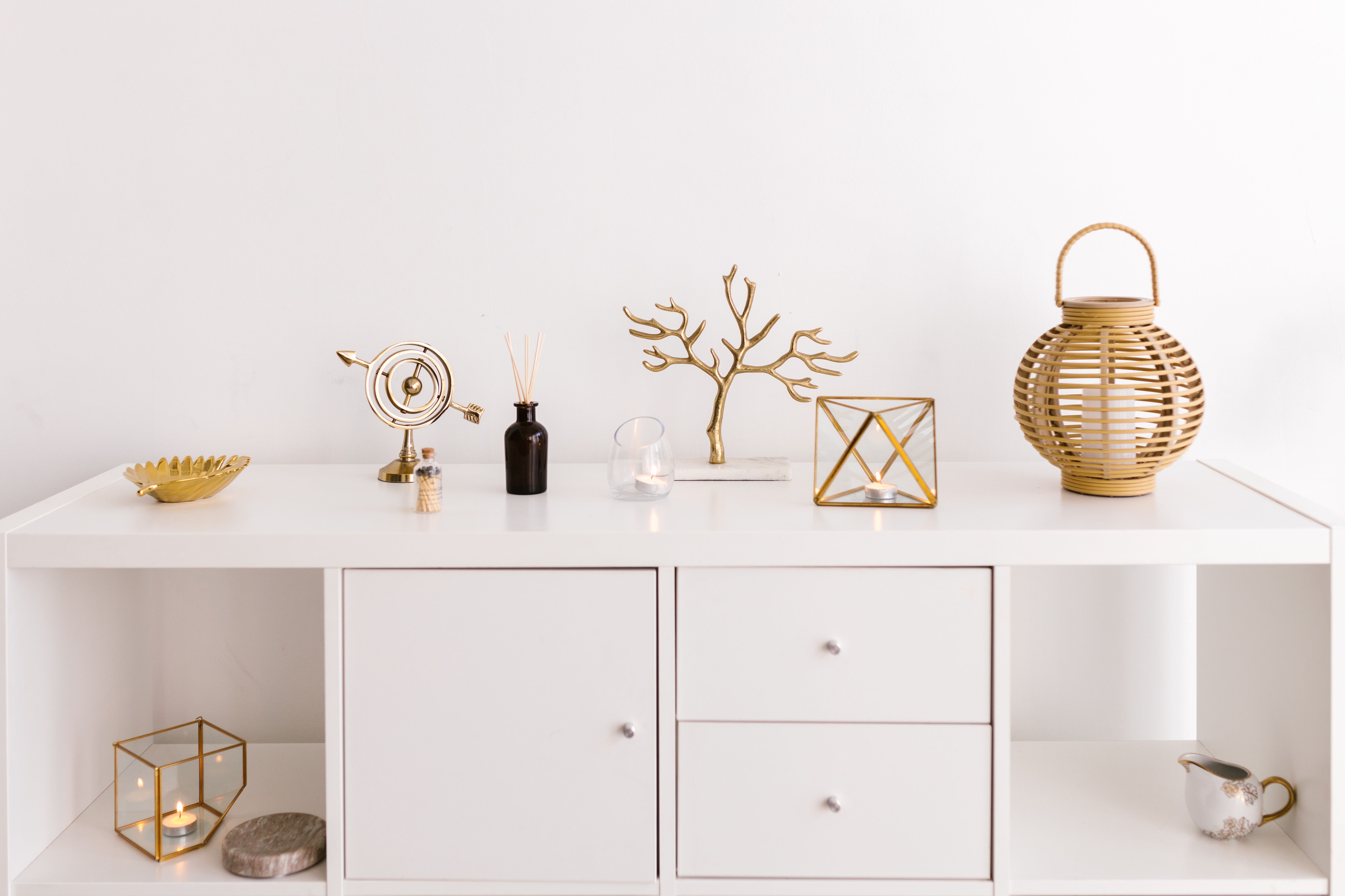 White console table styled with warm gold coral branch, geometric candle holder, and wicker lantern