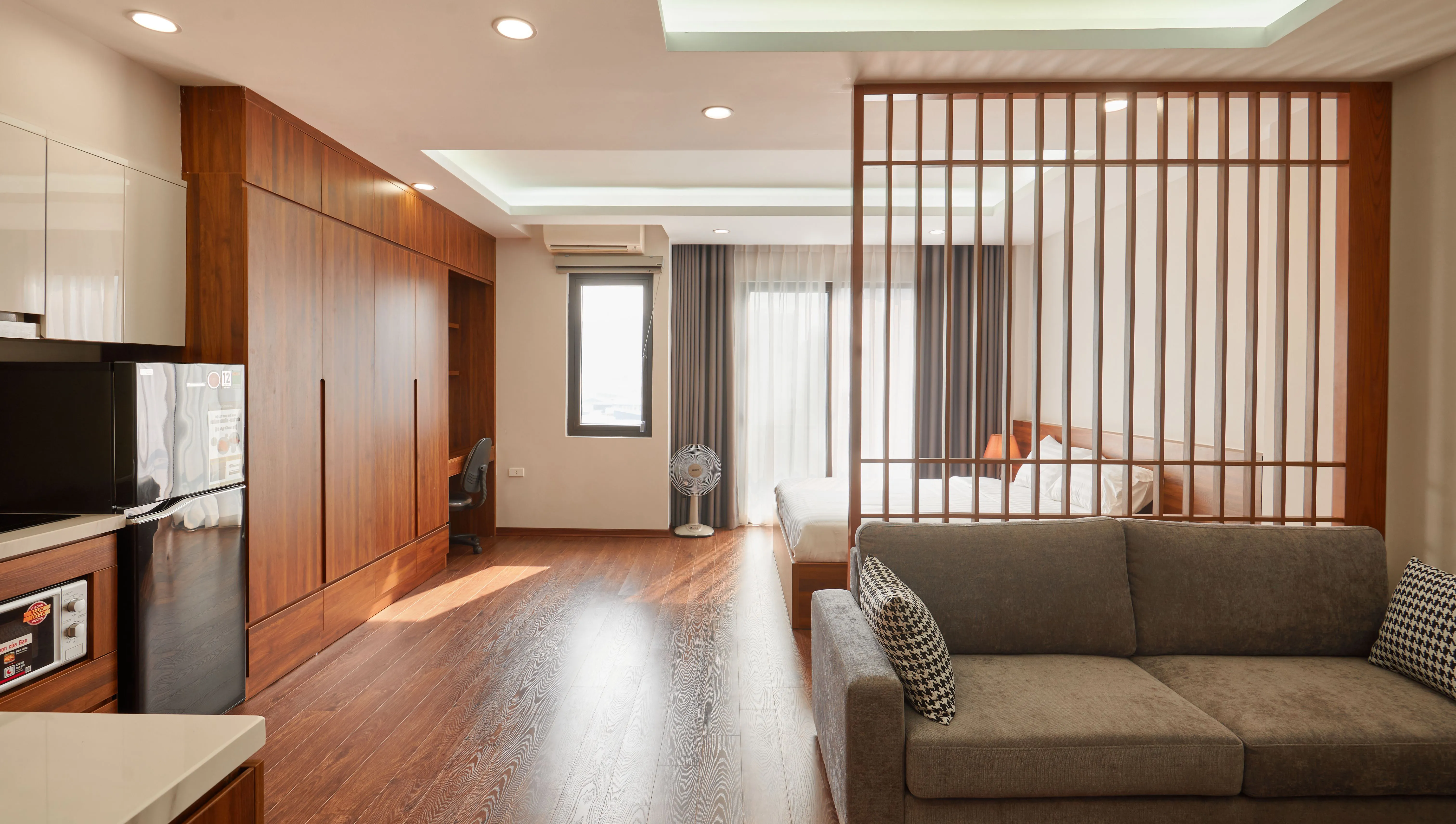 A modern studio apartment with a warm wood slat room divider separating the sleeping area from the living space