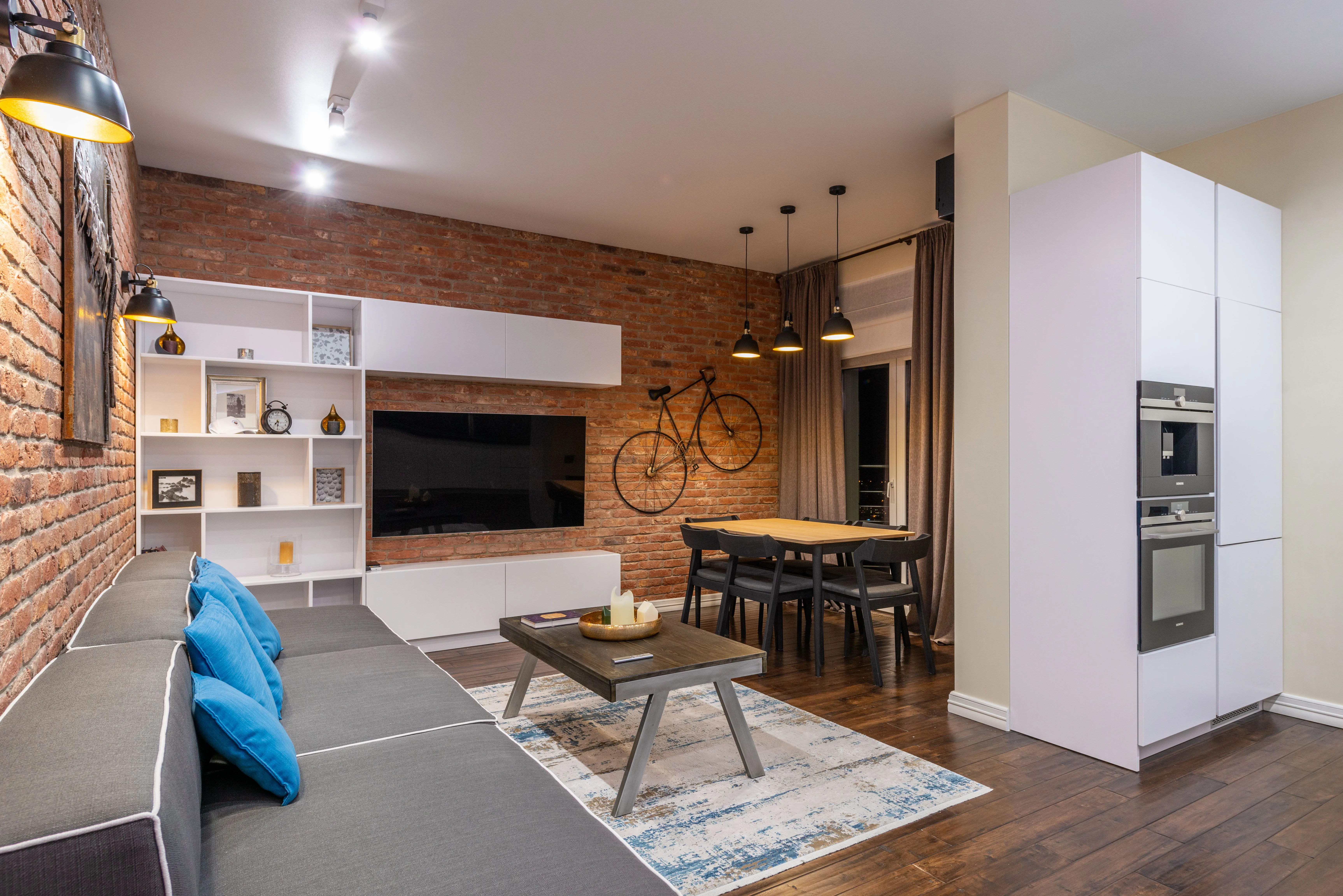 An industrial studio apartment with exposed brick, open living and dining zones, and warm pendant lighting
